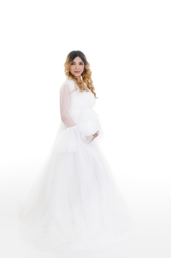 Vancouver Maternity and pregnancy photographer woman looking at camera while holding her belly in a white chiffon dress