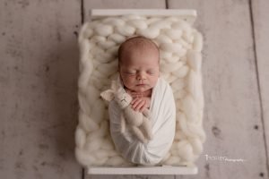 Newborn baby boy sleeping in a white bed holding a beige bunny