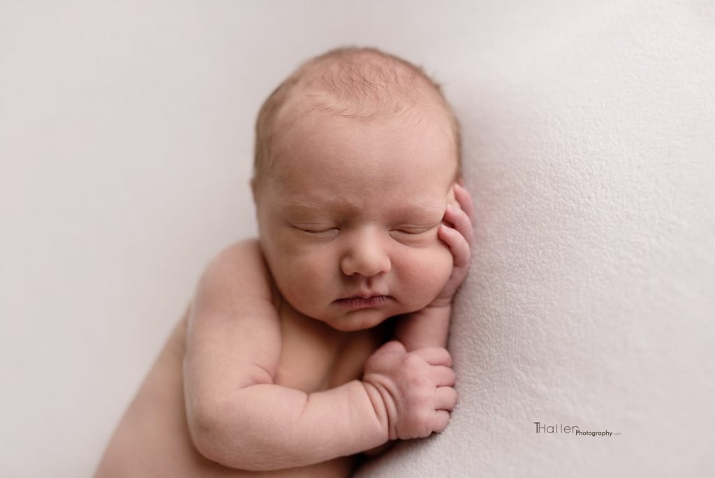 newborn baby holding his cheek while sleeping