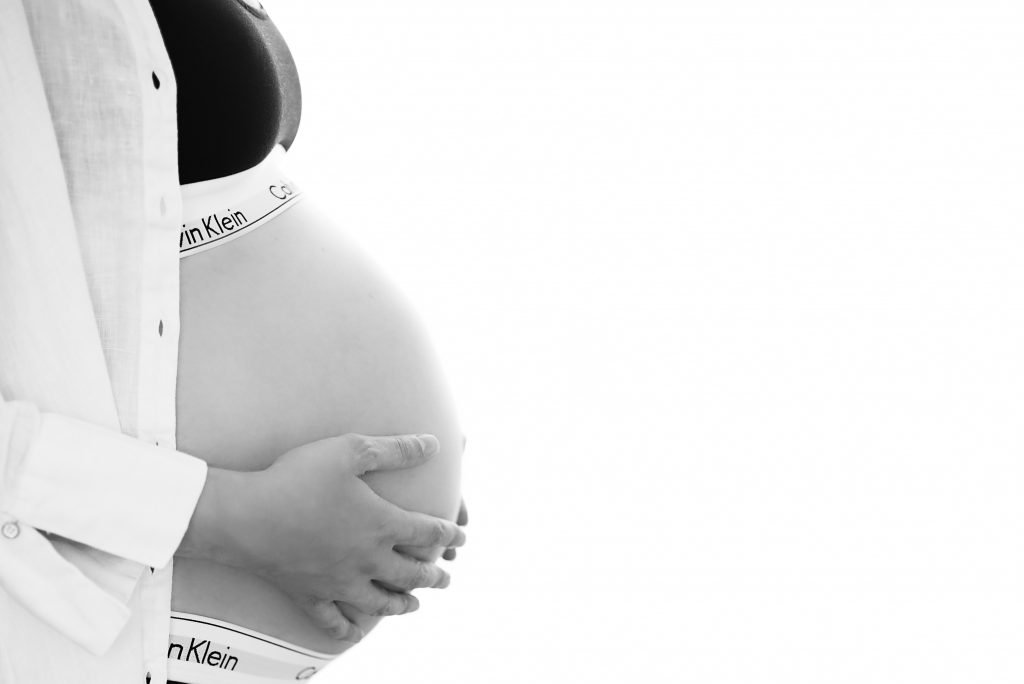 Sideview of a belly of a pregnant woman wearing Calvin Klein underwear and a white shirt