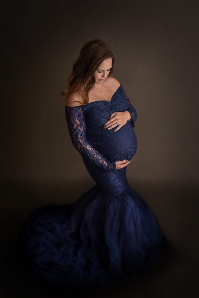 Woman holding her baby bump in a dark blue dress