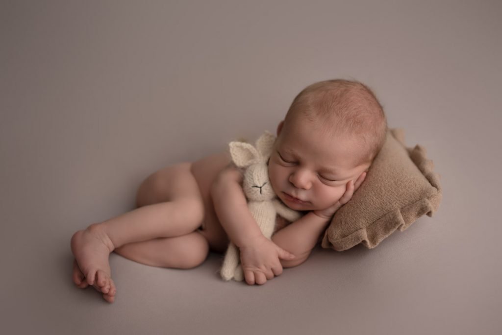 Newborn Baby boy sleeping on a little pillow holding a bunny