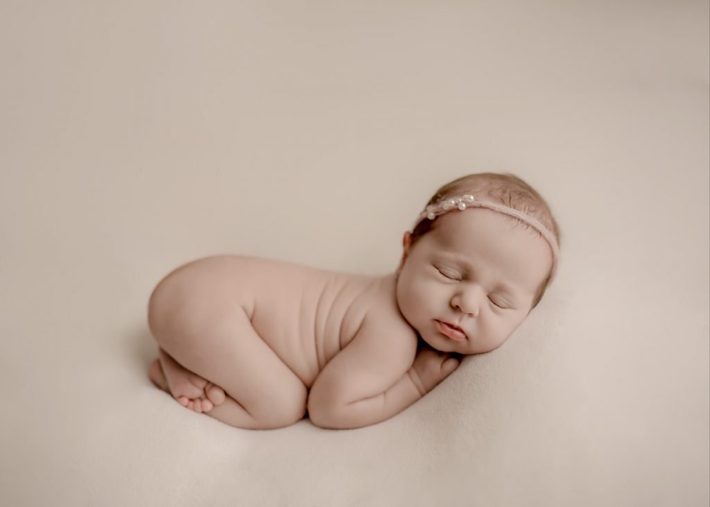 Newborn baby girl sleeping in bum up pose with pearl headband