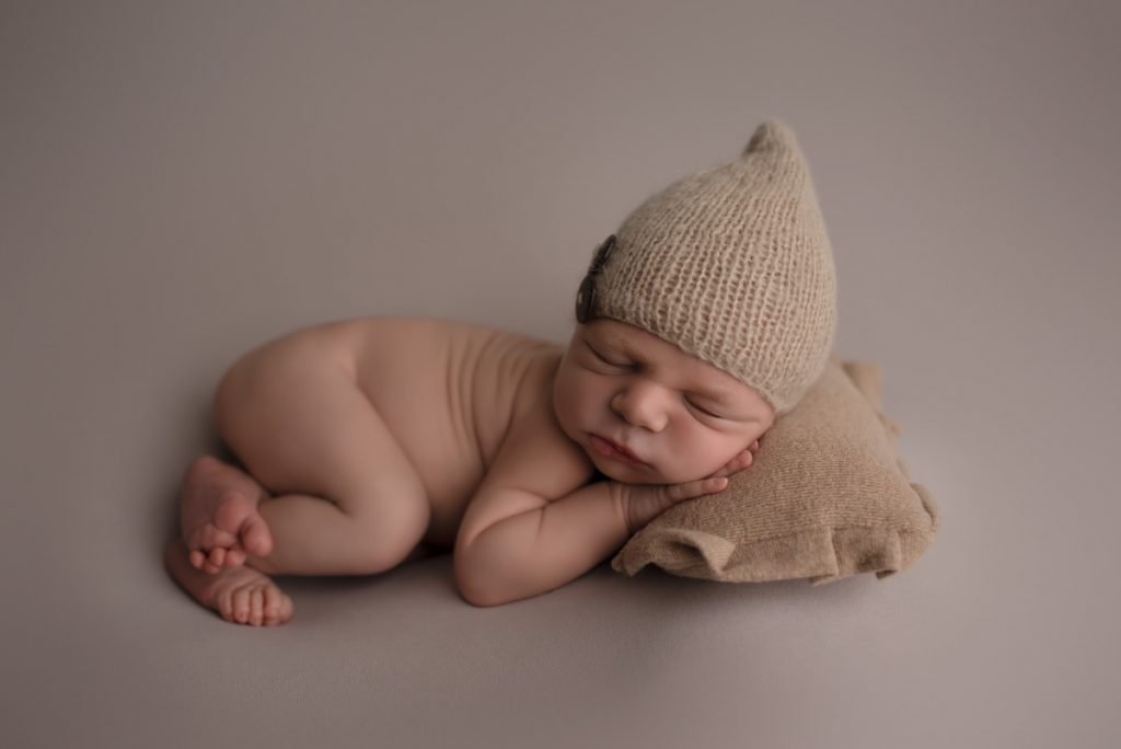Vancouver Newborn Photographer - Newborn boy sleeping on a pillow wearing a cute hat with buttons