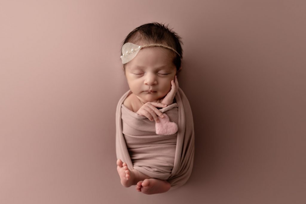 Vancouver Newborn Photoshoot - Baby girl holding a pink heart sleeping on a rose coloured backdrop