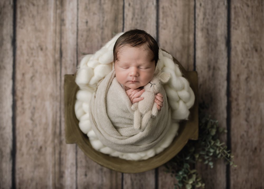 Newborn baby boy placed in a wooden bowl holding a little bunny sleeping