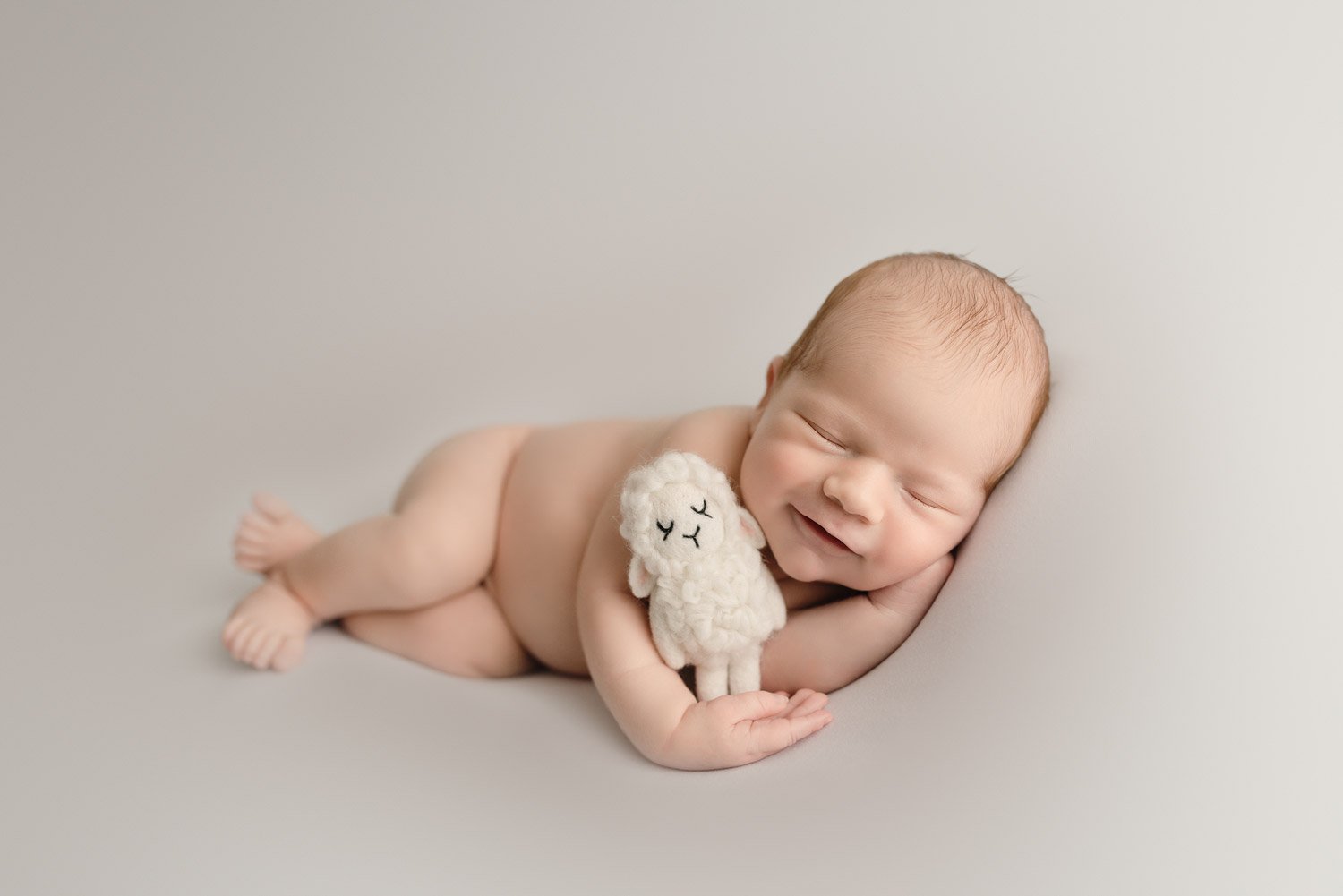 Vancouver Newborn Photography baby boy smiling sleeping while holding a toy sheep